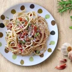 Un plato de espagueti aglio olio peperoncino, con ajo, perejil y un toque de tomate.
