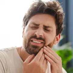 Hombre con expresión de dolor, tocándose la mejilla por una caries muela.