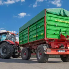 Czerwony traktor ciągnie zieloną przyczepę. Dowiedz się, jakich przyczep nie trzeba rejestrować, by ułatwić sobie pracę w gospodarstwie.