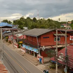 Un pueblo en el Mae Hong Son Loop, con casas rojas y azules a lo largo de una carretera, rodeado de exuberante vegetación y un cielo nublado.