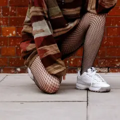 Osoba w swetrze w pasy i białych sneakersach, prezentująca, co to kabaretki – czarne, siateczkowe rajstopy.