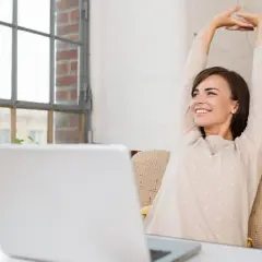 Frau streckt sich glücklich vor ihrem Laptop. Endlich Zeit für die 45-minütige Pause.