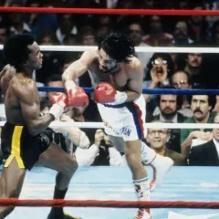 Sugar Ray Leonard lands a punch on Roberto Duran in a fierce boxing match. The crowd watches intently as the two legends battle in the ring.