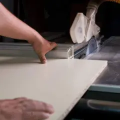 Ręce prowadzą płytę meblową do piły tarczowej, pokazując, czym ciąć płytę meblową.