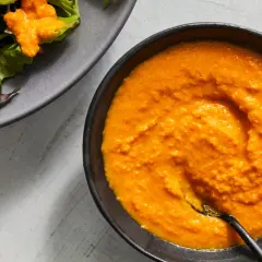 A vibrant bowl of carrot ginger dressing sits next to a salad with cucumber slices.