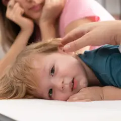 Małe dziecko z blond włosami leży na białym materacu, jego mama patrzy z troską. Czy to początek pandas choroba?