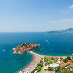 Sveti Stefan, Czarnogóra, z widokiem na turkusowe morze i zatłoczoną plażę.
