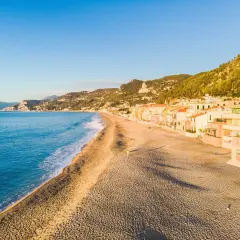 Plage de sable fin bordée de maisons colorées sur la côte italienne. La mer bleue et les collines verdoyantes complètent ce paysage paisible.