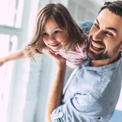 Ojciec trzyma córkę na rękach, oboje śmieją się radośnie. To piękny obrazek rodziny po angielsku.
