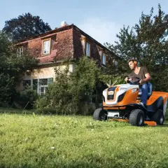 Mężczyzna na pomarańczowo-białej kosiarce samojezdnej STIHL radzi sobie z nierównym terenem. Idealny traktorek kosiarka na nierówny teren.