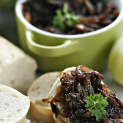 Chrupiące pieczywo z aromatyczną, ciemną cebulą karmelizowaną, ozdobione natką pietruszki. Obok surowa cebula i kawałki bagietki.