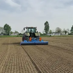 Trattore verde in azione per l'erpicatura del terreno, preparando il campo per la semina.