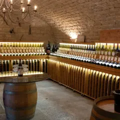 Cave voûtée du **domaine de Montmain** avec étagères en bois illuminées présentant de nombreuses bouteilles de vin, tonneaux et lustre ancien.