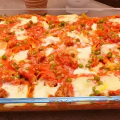 Nidi di tagliatelle al forno con ragù, piselli e mozzarella filante, un piatto invitante e saporito.