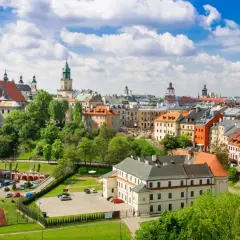 Widok na zabytkowe centrum Lublina, z charakterystycznymi kamienicami i wieżami kościelnymi, otoczone zielenią. Lubelszczyzna w pełnej krasie.