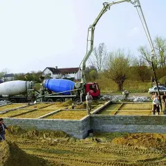 Betonowanie ławy fundamentowej. Dwie betoniarki i pompa do betonu pracują na budowie.