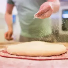 Ręka posypuje ciasto na pizzę mąką. Odpowiednia jaka mąka do pizzy to klucz do sukcesu.