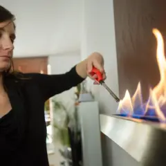 Frau zündet Ethanol-Kamin an. Die Flammen tanzen, ein Zeichen für Wärme und Gemütlichkeit, dank der Ethanol-Marke.