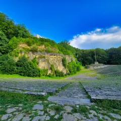 Amfiteatr na Górze Świętej Anny, otoczony zielenią, z kamiennymi ławami i monumentem.