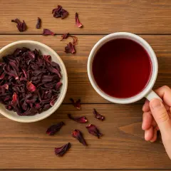 Suszone kwiaty hibiskusa w miseczce i filiżanka czerwonego naparu. Odkryj hibiskus właściwości i ciesz się jego smakiem.