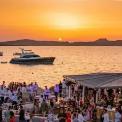 Tramonto dorato su un phi beach affollato, con yacht e bar sulla spiaggia.