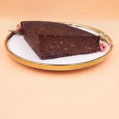 Czekoladowy brownie z bananami i masłem orzechowym, ozdobione suszonymi kwiatami, na talerzu ze złotym rantem.