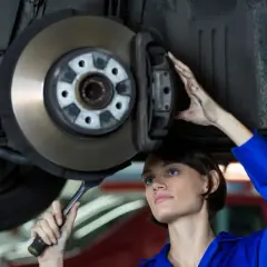 Mechaniczka w niebieskim kombinezonie wykonuje wymianę tarcz hamulcowych, trzymając klucz.