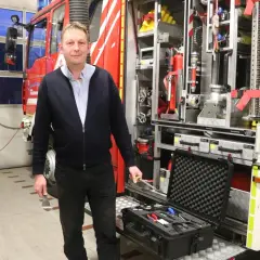 Mann vor Feuerwehrfahrzeug mit Werkzeugkoffer. Tolle Feuerwehr mitgliederwerbung ideen für Nachwuchs.