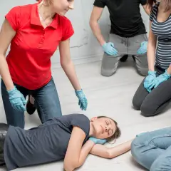 Erste-Hilfe-Kurs: Eine Frau wird in die stabile Seitenlage gebracht. Mehrere Personen mit blauen Handschuhen beobachten aufmerksam.