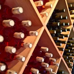 Scaffale in legno con bottiglie di vino rosse e scure, disposte con la corretta inclinazione per la conservazione.