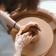 Dłonie artysty formują glinę na kole garncarskim. Powstaje piękna, ręcznie robiona pottery.