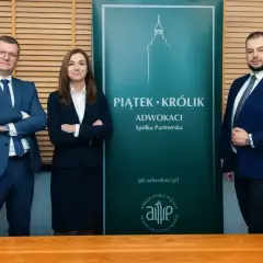 Trzech prawników w garniturach stoi przed zielonym banerem kancelarii "Piątek Królik Adwokaci".