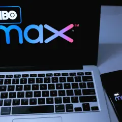 Logo HBO Max na ekranie laptopa i smartfona, obok słuchawki.