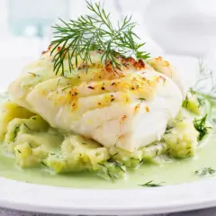 Pyszna ryba w sosie koperkowym, podana na purée ziemniaczanym z dodatkiem koperku. Danie ozdobione świeżym koperkiem.