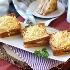Tre gyllene croque monsieur, gratinerade med ost, ligger uppradade på en vit bricka. En klassisk fransk delikatess.