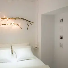 Ideas para decorar ramas secas: una rama con luces cálidas sobre la cama, fotos y mariposas en la pared.