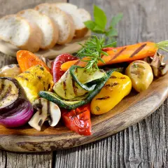 Légumes grillés colorés sur une planche en bois, accompagnés de pain frais. Un filet de crème de balsamique sublimerait ce plat.