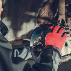 Mechanik w czerwonych rękawicach pracuje przy hamulcach, przygotowując wymianę przewodów hamulcowych.