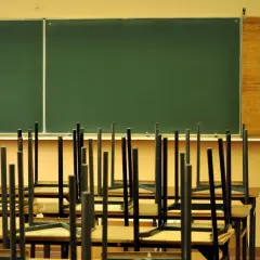 Puste krzesła odwrócone na ławkach przed zieloną tablicą w sali lekcyjnej.