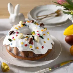 Wilgotna babka bez jajek, ozdobiona lukrem, kolorowymi drażetkami i czekoladowymi jajeczkami, na wielkanocnym stole.