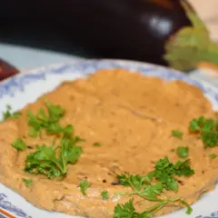 En krämig baba ganoush, garnerad med persilja, med aubergine och citron i bakgrunden.