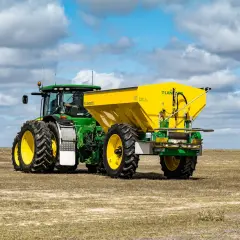 Zielony John Deere 7810 z żółtym rozsiewaczem Landaco T130 na polu.