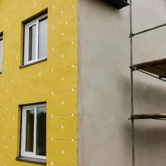 Edificio in fase di isolamento con cappotto termico giallo. L'estate è il momento ideale per questi lavori che garantiscono comfort e risparmio energetico.