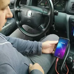 Mężczyzna w samochodzie podłącza telefon do radia, by uzyskać połączenie telefonu z samochodem. Na ekranie telefonu widnieje logo Weblink.