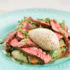 Skivad flankstek Morberg med potatis och en klick potatispuré, garnerad med örter.
