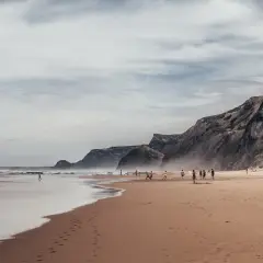 Plaża w Faro, wrzesień. Ludzie grają w piłkę, spacerują po piasku. W tle skaliste klify i ocean.