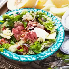 En härlig ost och skinksallad med melon, tomater och pinjenötter. Serveras på en vacker turkosblå skål.