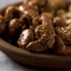 Un tazón de madera lleno de piñones garrapiñados, con un brillo dulce y apetitoso.