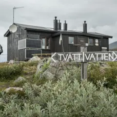 Vandrare närmar sig en av kungsleden stugor. En skylt pekar mot "TVÄTT VATTEN".