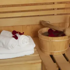 Białe ręczniki i drewniane wiaderko z wodą i płatkami róż w saunie. Dylemat: najpierw sauna sucha czy parowa?